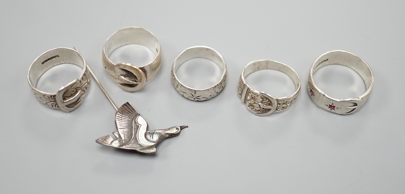 Four assorted silver buckle rings, including one set with red stones, an engraved silver band and a 925 duck stick pin.
